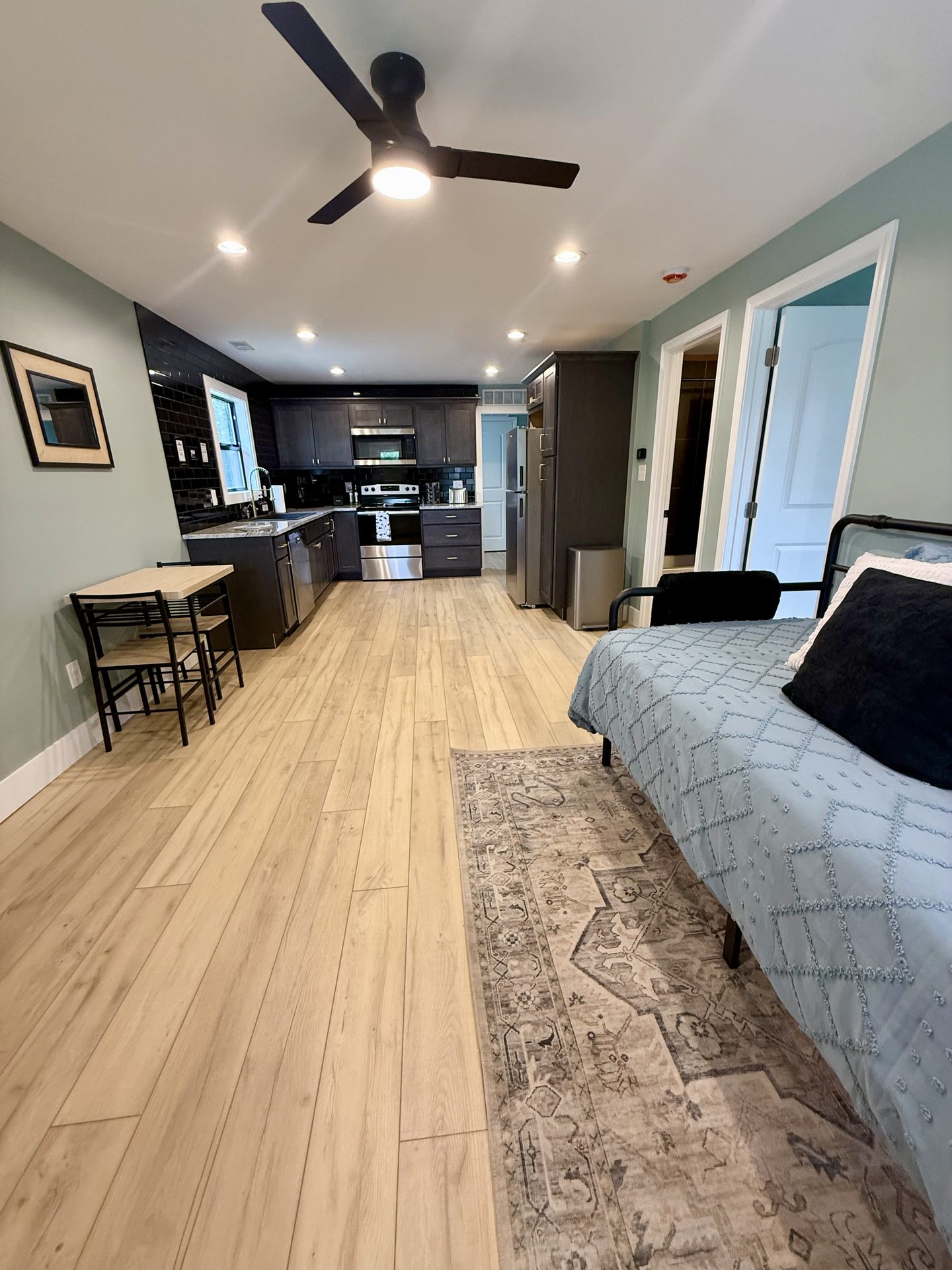 Open-plan room looking down light wood flooring toward a dark-cabinet kitchen, with a sofa and a dining table