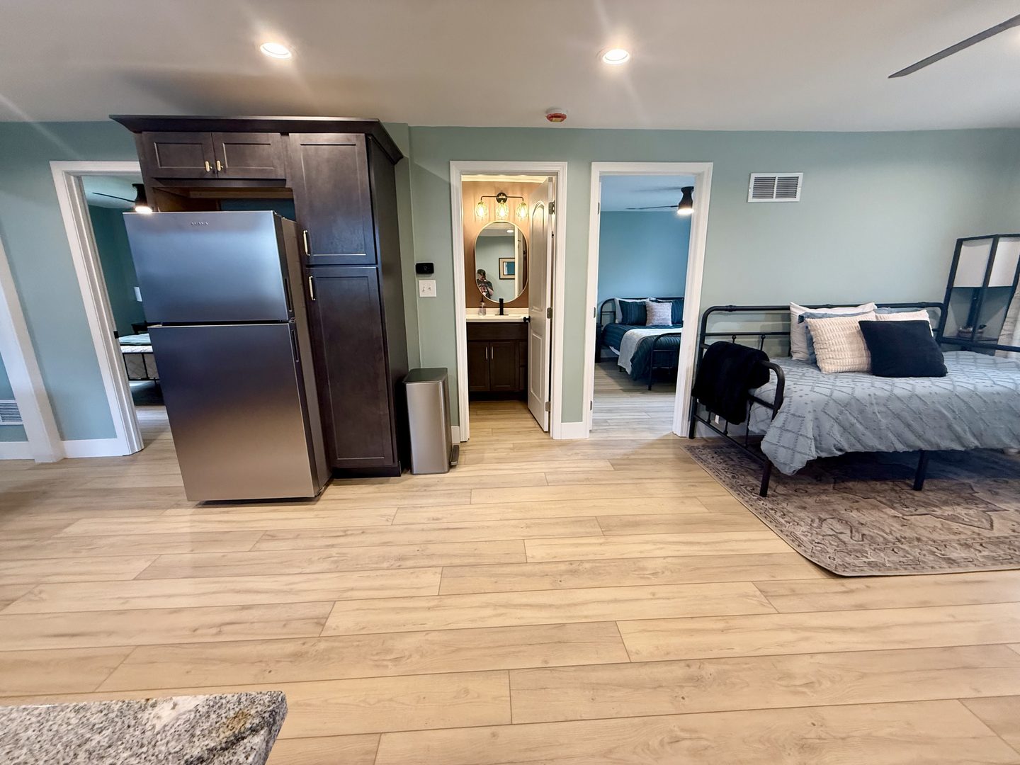 Wide view of the open-plan room with the kitchen, a queen bed area and doors to both bathrooms