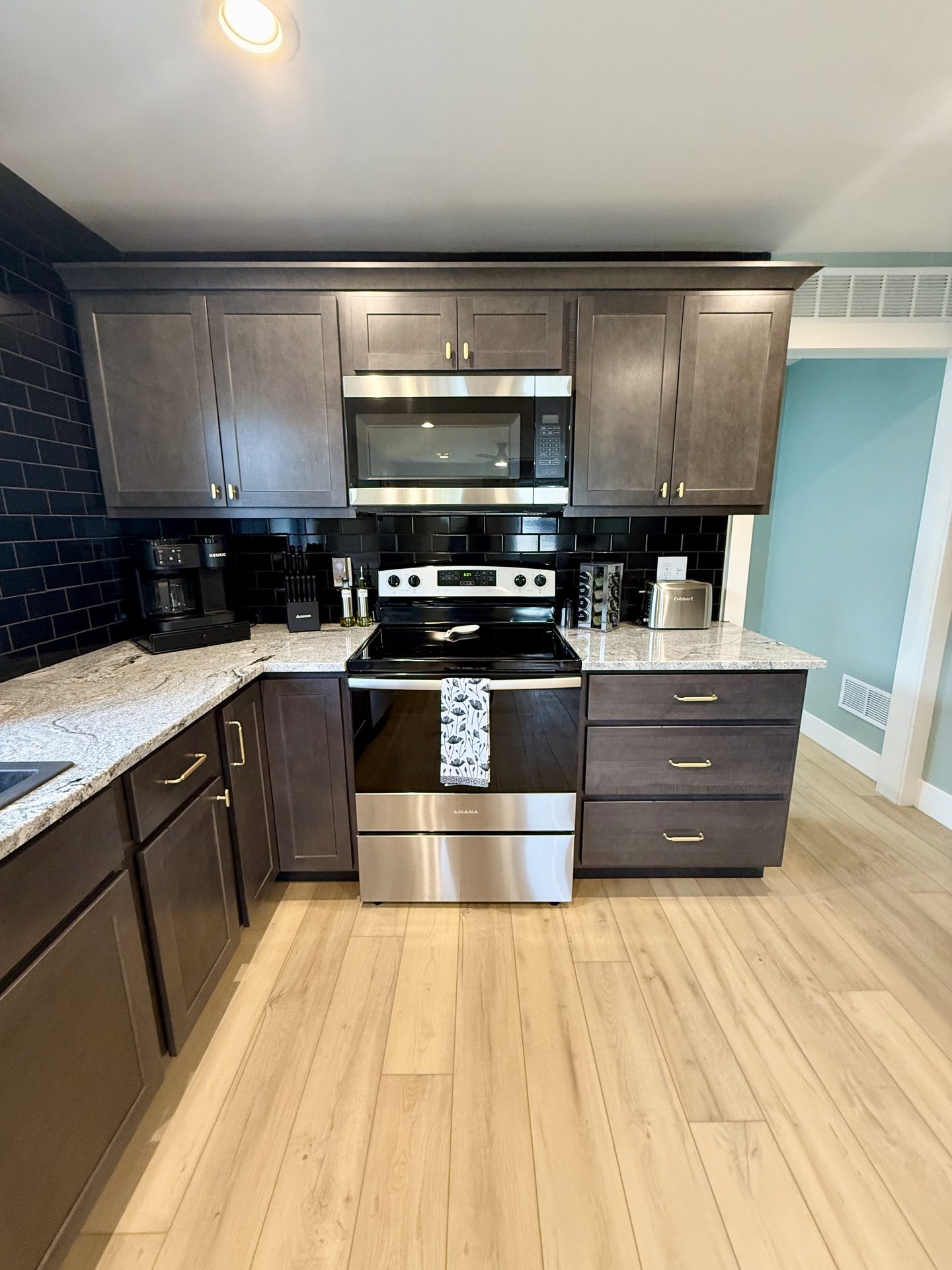 Kitchen with dark shaker cabinets, granite counters, a black subway-tile backsplash and stainless appliances