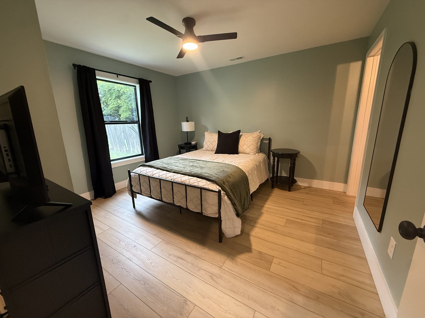 Second green bedroom with a queen bed and a tall arched mirror
