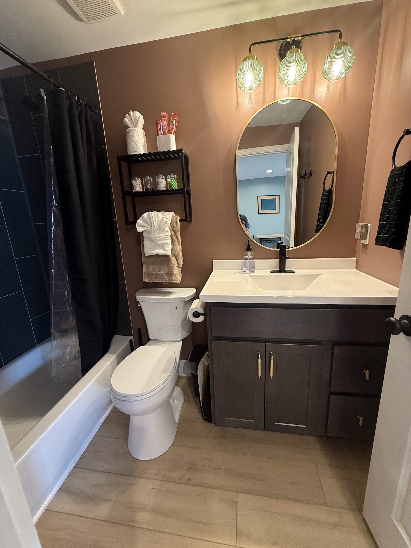 Bathroom with a tub and shower, a dark vanity with a white top, a round gold mirror and folded towels