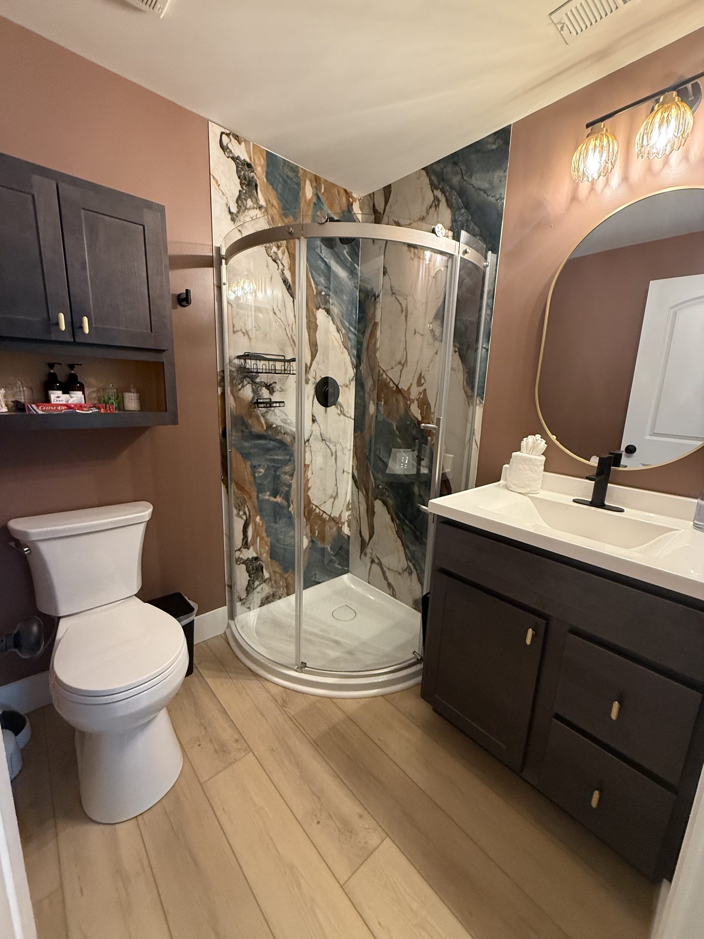 Bathroom with a curved glass shower, a marble-look surround and a dark vanity