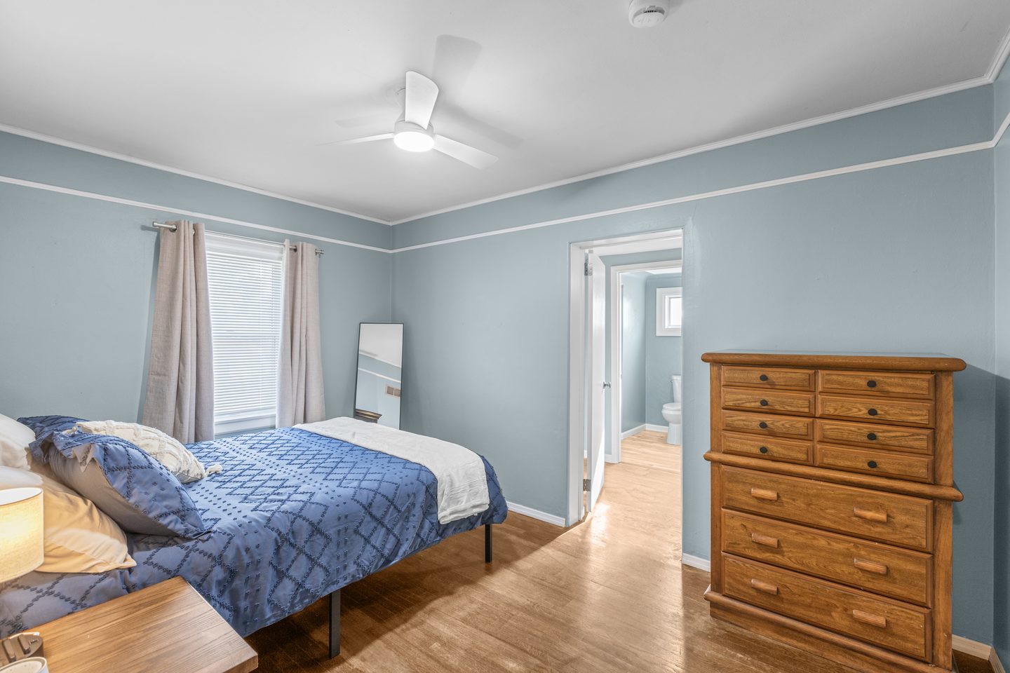 The blue bedroom from the other side, with a wooden dresser and a door through to the hall