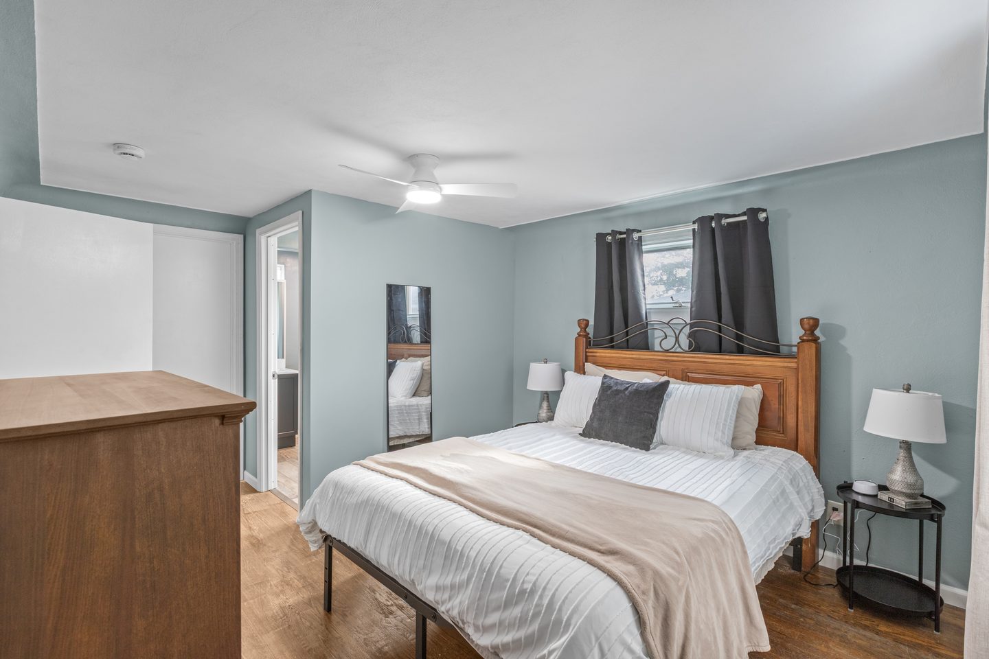 Bedroom with a queen bed in white bedding, a wooden headboard, two lamps and dark curtains