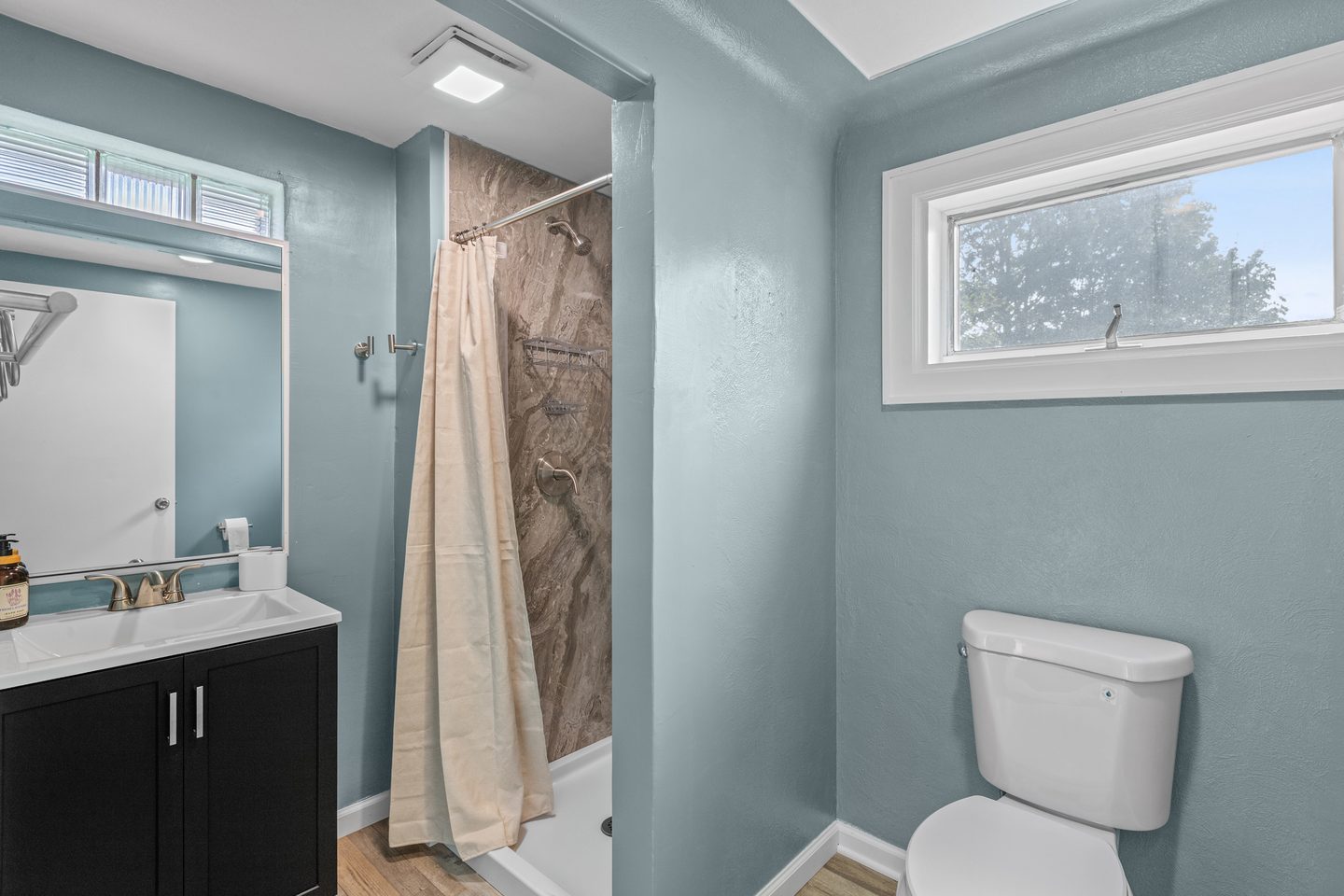 Bathroom with a shower, a black vanity and a high window