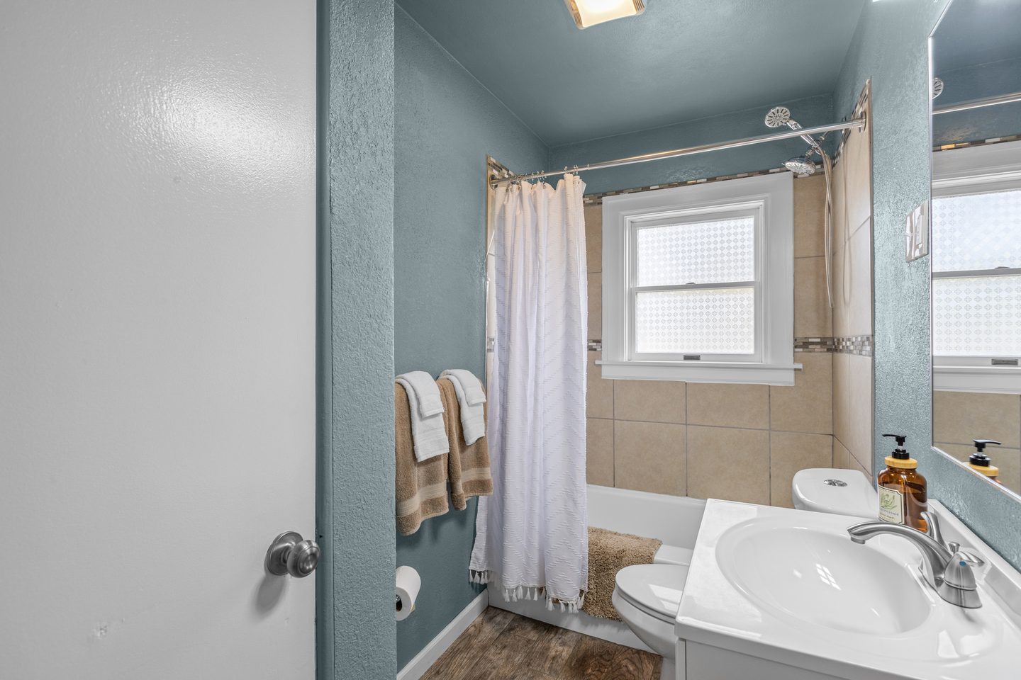 Bathroom with a tub and shower curtain, a white vanity and a frosted window