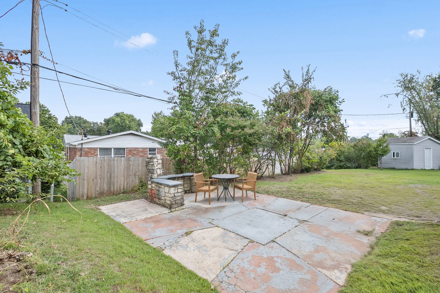 Stone patio with a fire pit, a bistro table and chairs, and a fenced lawn