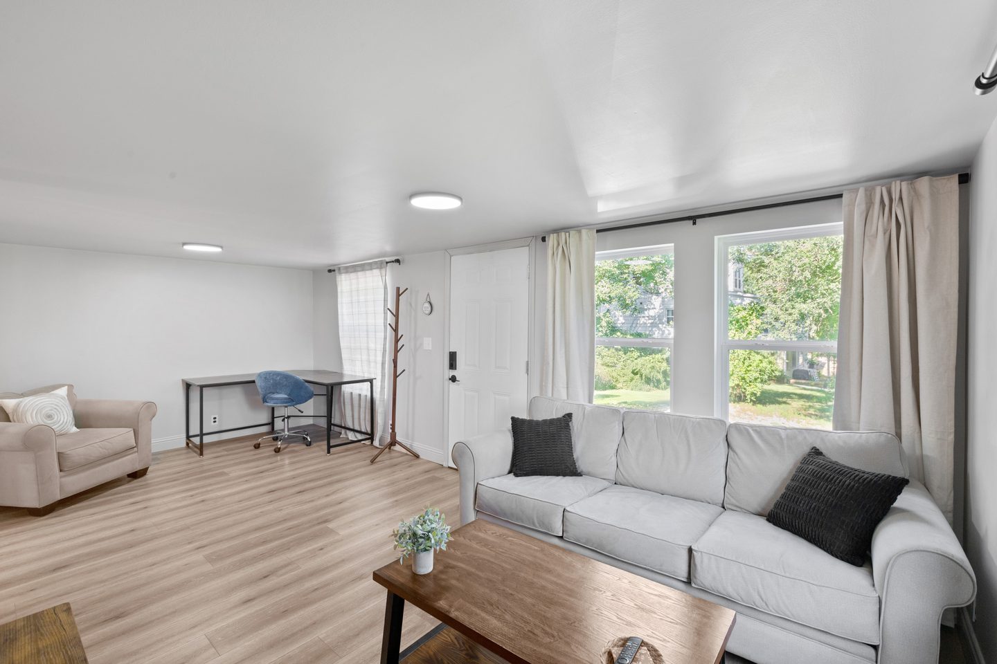 Living room with a grey sofa, a wood coffee table and a desk with an office chair by the front window