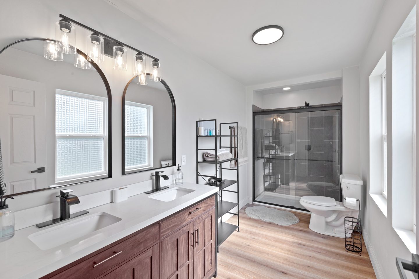 Bathroom with a double vanity under two arched mirrors and a glass-walled shower