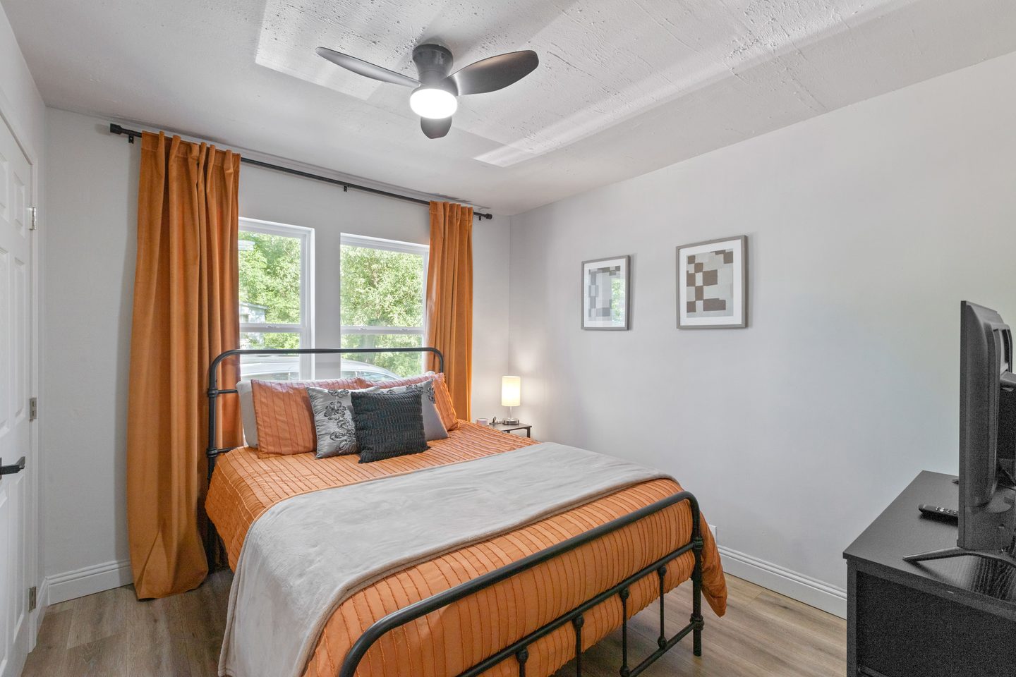 Bedroom with a queen bed in orange bedding, orange curtains and a ceiling fan