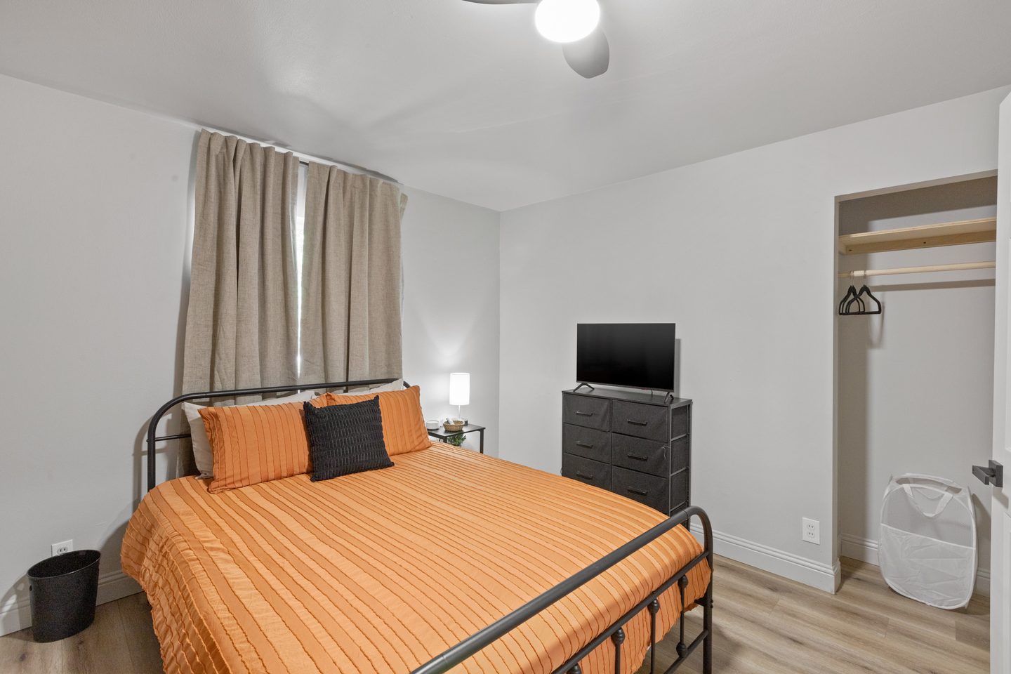 Bedroom with a queen bed in orange bedding, a dresser with a television and an open closet