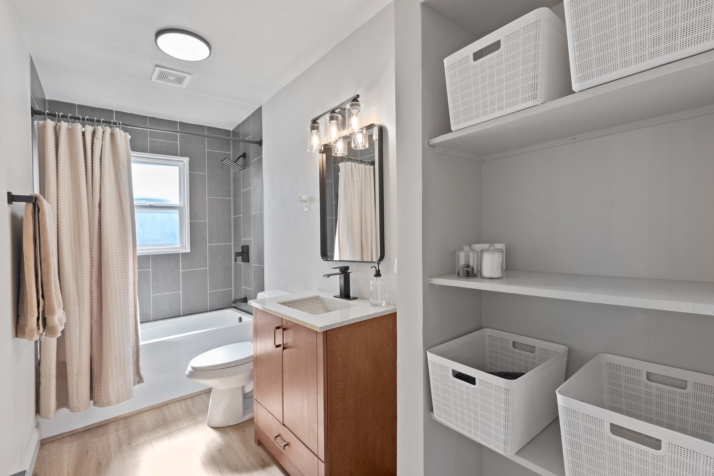 Bathroom with a tub and shower, a wood vanity and open shelving with storage baskets
