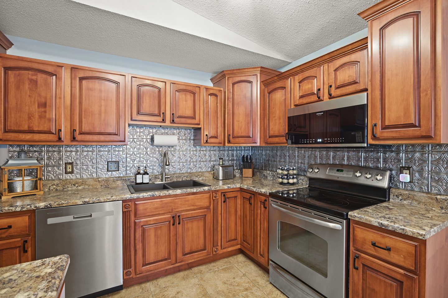 Kitchen with cherry cabinets, granite counters, a pressed-tin backsplash and a stainless range, microwave and dishwasher
