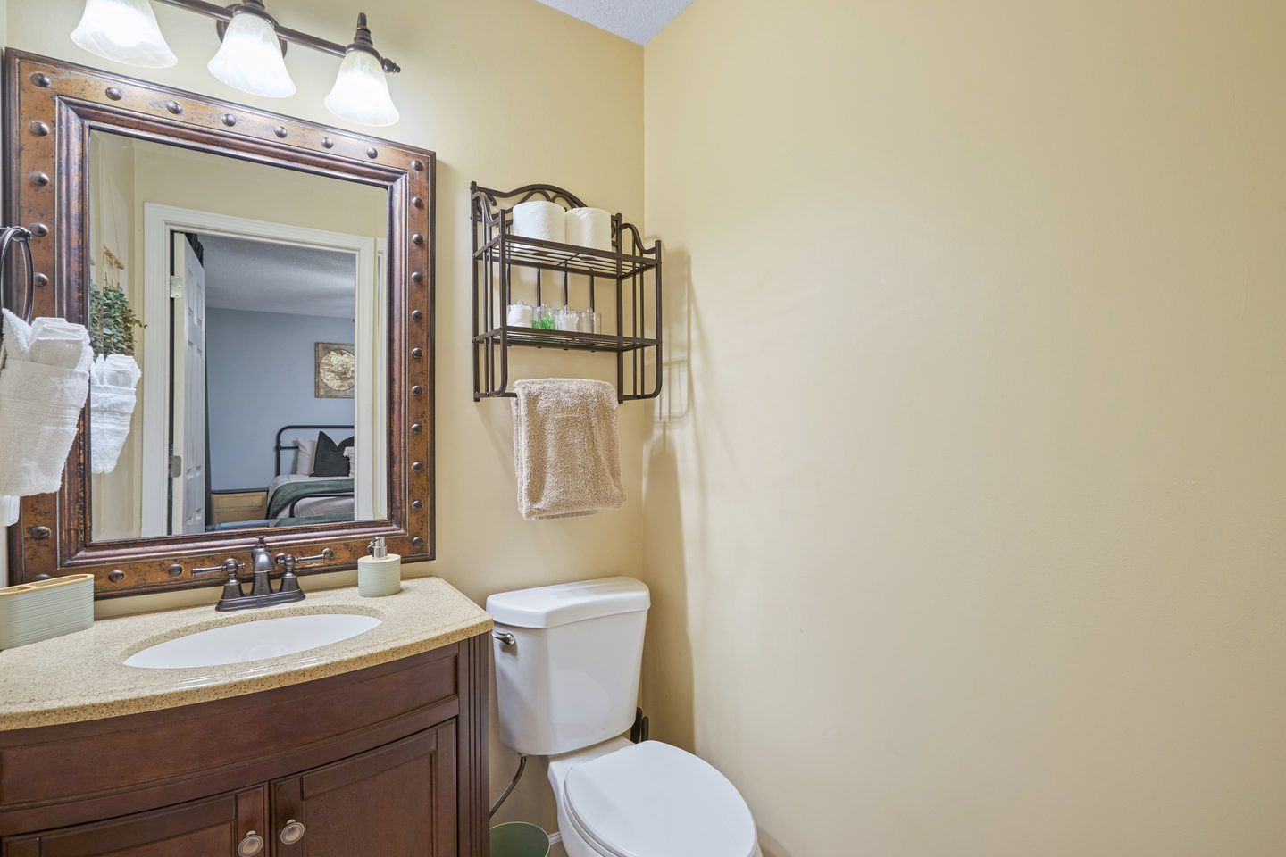 Half bathroom with a wood vanity, a framed mirror, a towel shelf and warm yellow walls