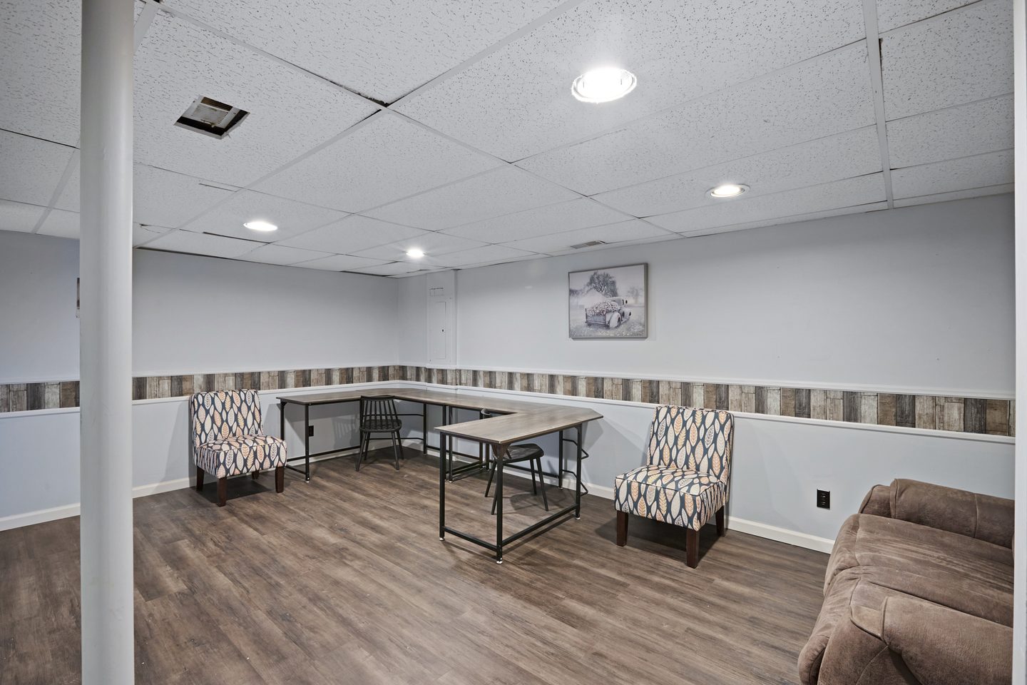 Finished lower-level bonus room with wood-look flooring, a desk, two armchairs and a sofa