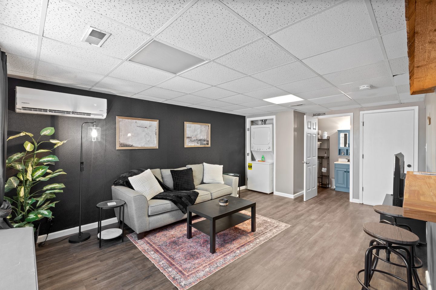 Living room with a dark feature wall, a grey sofa, a coffee table on a rug and a wall-mounted air conditioner