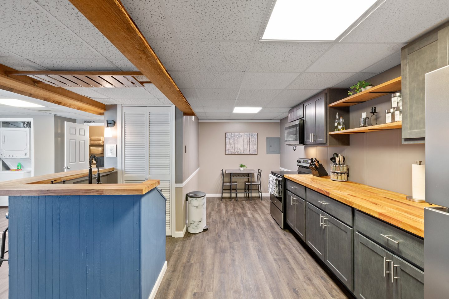 Galley kitchen with butcher-block counters, grey cabinets, open shelving and a blue-panelled breakfast bar