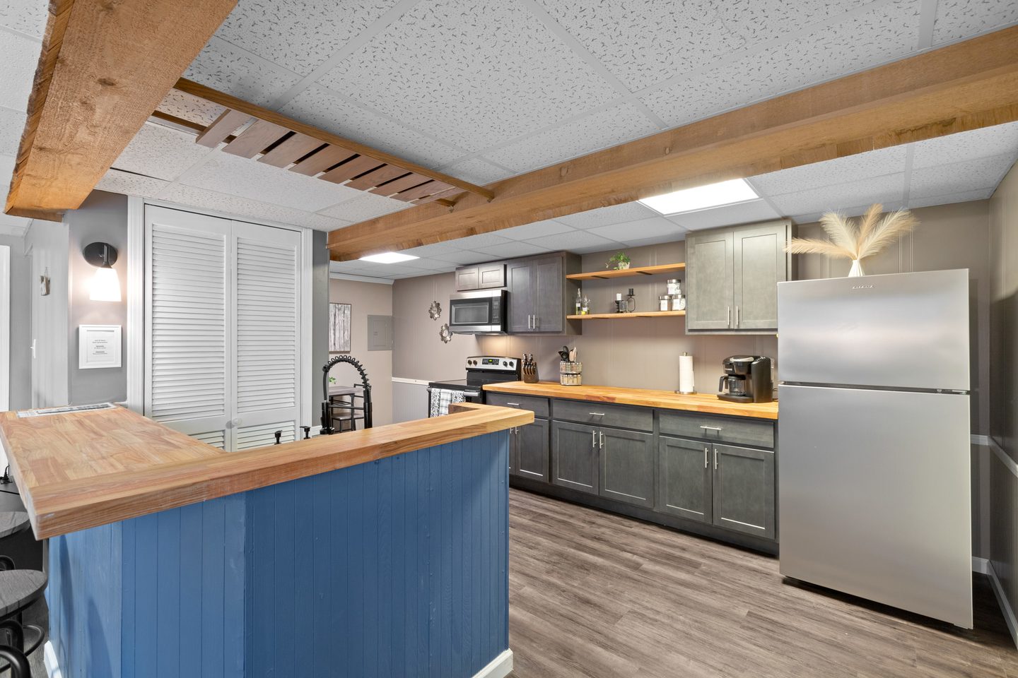 Kitchen with exposed wooden beams, a stainless refrigerator and butcher-block counters running the length of the room