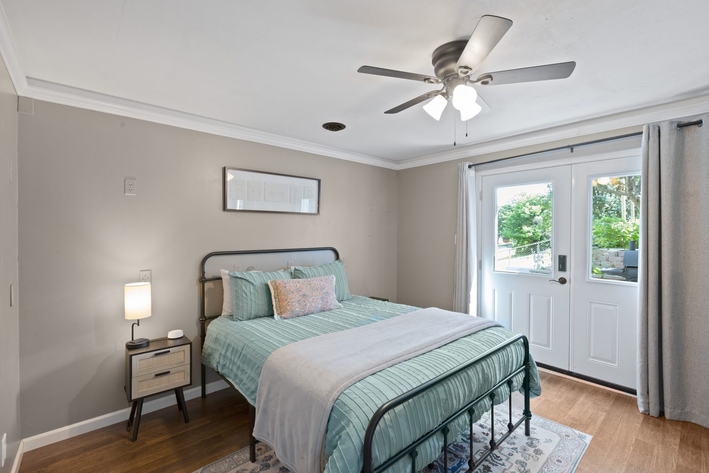 Bedroom with a queen bed in mint bedding on a black metal frame, and French doors opening onto the patio