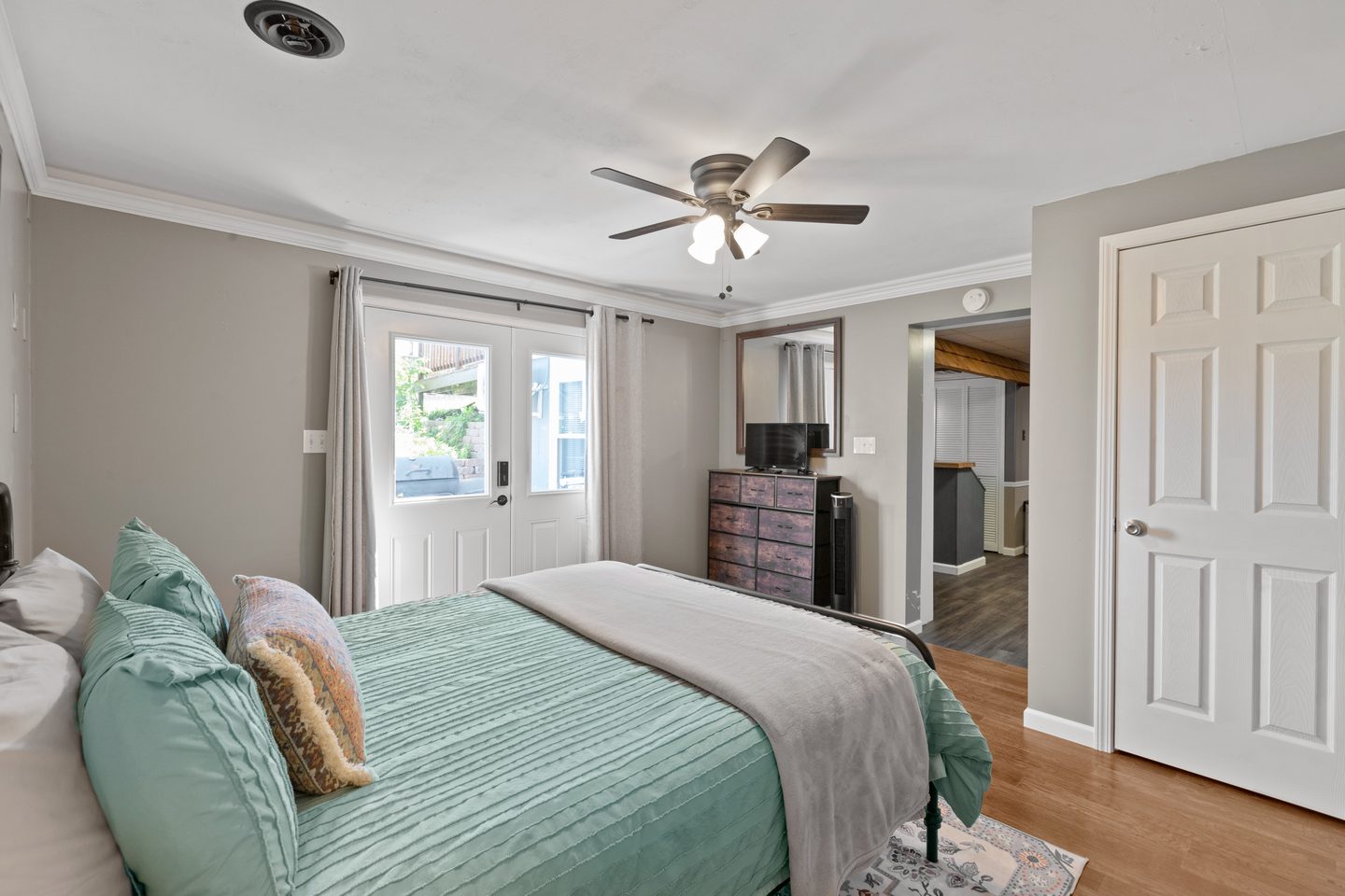Bedroom with a queen bed in mint bedding, a nightstand with a lamp and a ceiling fan