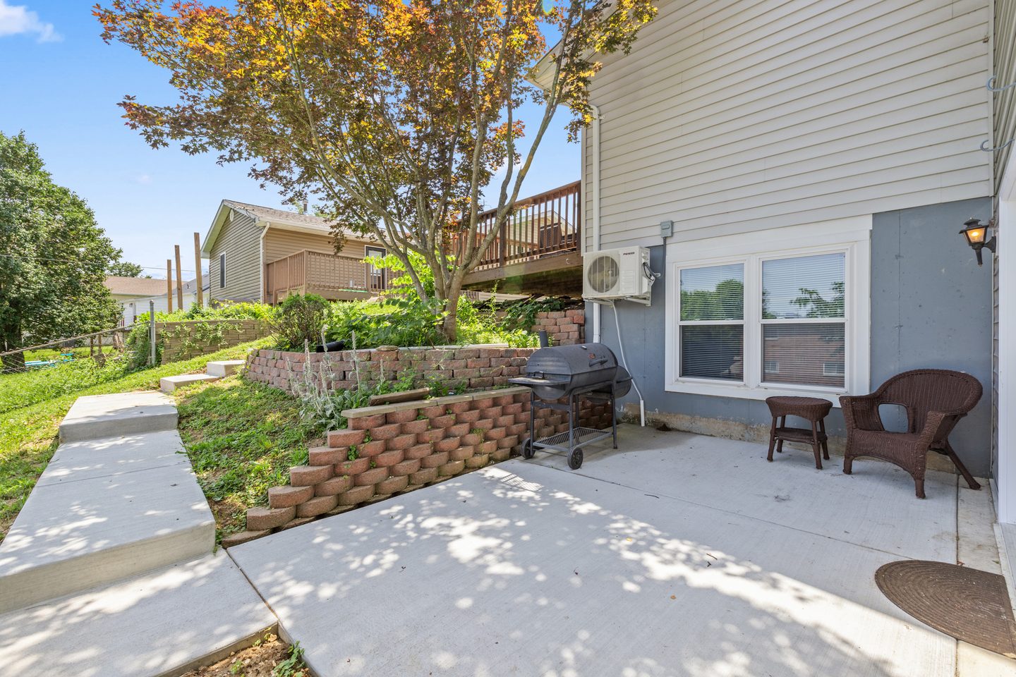 Concrete patio with a charcoal grill and two wicker chairs beside the apartment's own entrance