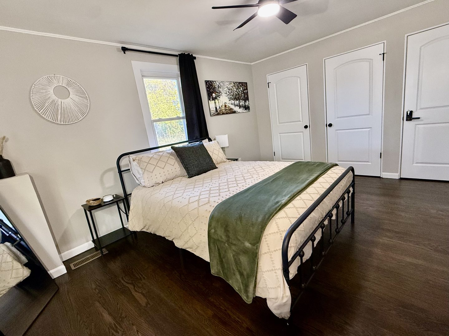 Bedroom with a queen bed in cream bedding, a green throw and a sunburst wall decoration