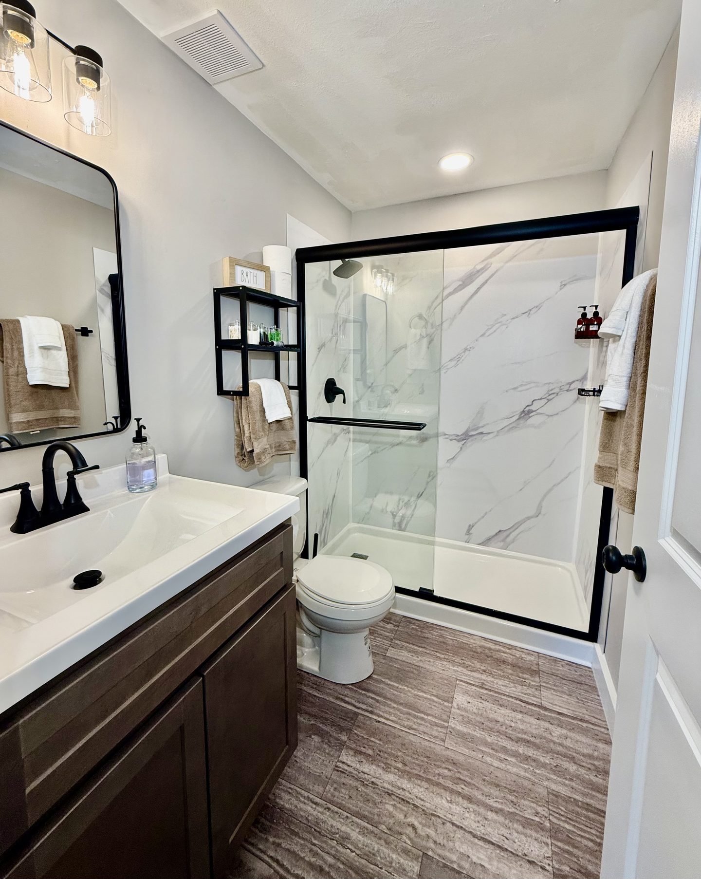 Bathroom with a glass-walled shower, a marble-look surround and a dark vanity