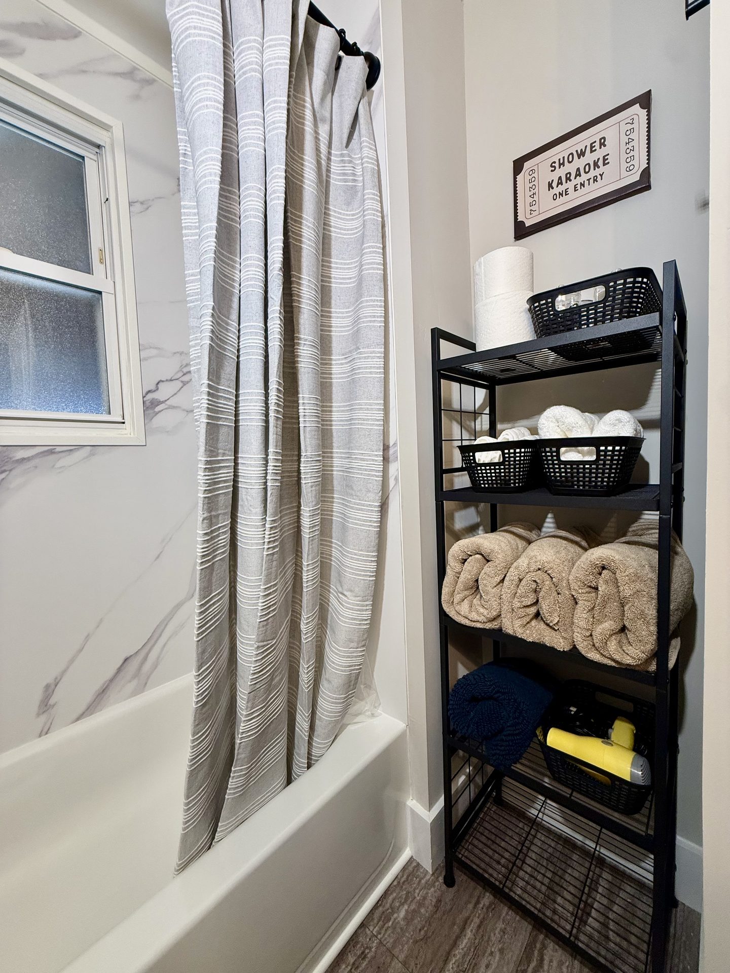 Bathroom with a tub and shower curtain beside a shelf of rolled towels