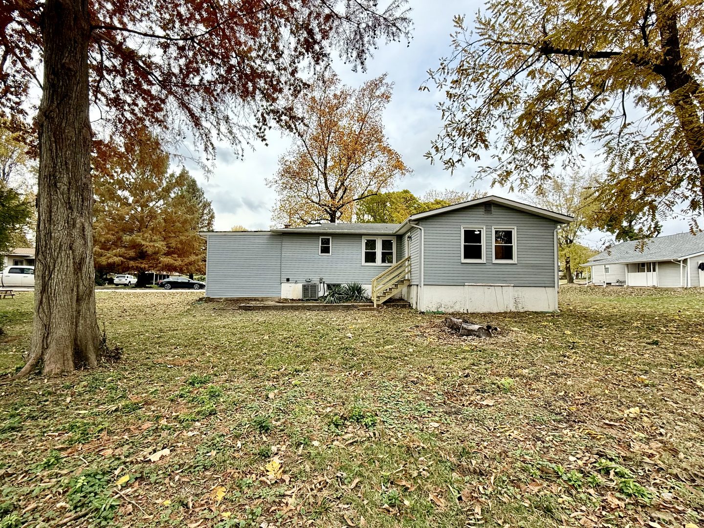 Single-storey house with grey siding behind a large lawn under autumn trees